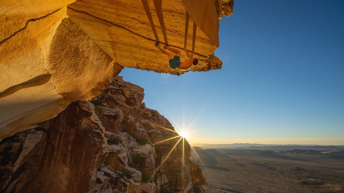 A man climbs a mountain edge as the sun sets in The Soloist VR.