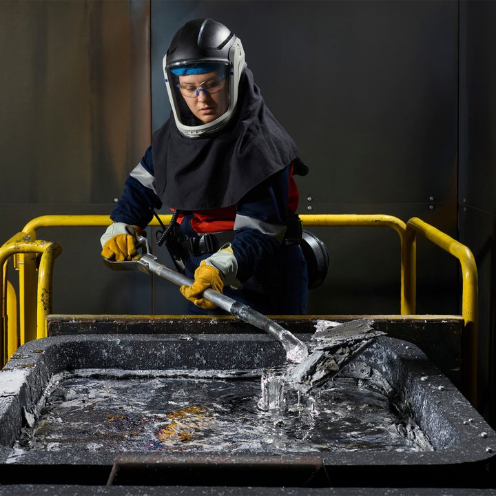 A woman mixes aluminum in a smelter.