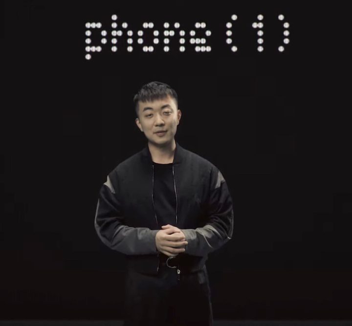 Carl Pei stads beneath Nothing Phone 1 logo.