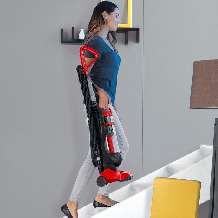 Woman carrying Dirt Devil Power Express Upright Bagless Vacuum up stairs.