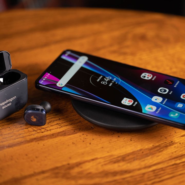 Motorola Edge+ (2022) on a Motorola charging pad next to Snapdragon earbuds on a wood table.