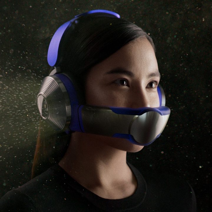 A woman wears the Dyson Zone air-purifying headphones against a black background filled with dust particles.