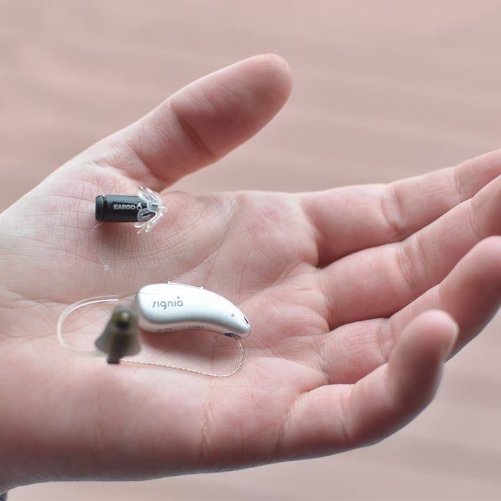 A hand holds an Eargo hearing aid and a Signia Pure C&G T AX hearing aid.
