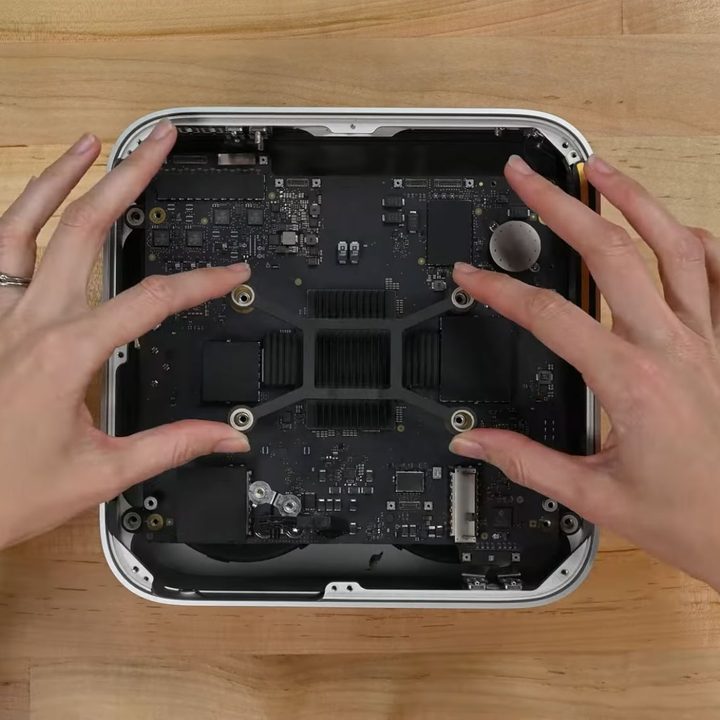 An iFixit engineer tearing down Apple's Mac Studio by removing a heatsink bracket.
