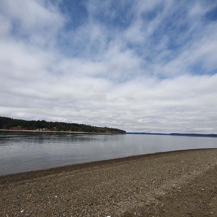 A rocky beach next to calm water under a blue sky streaked with clouds.