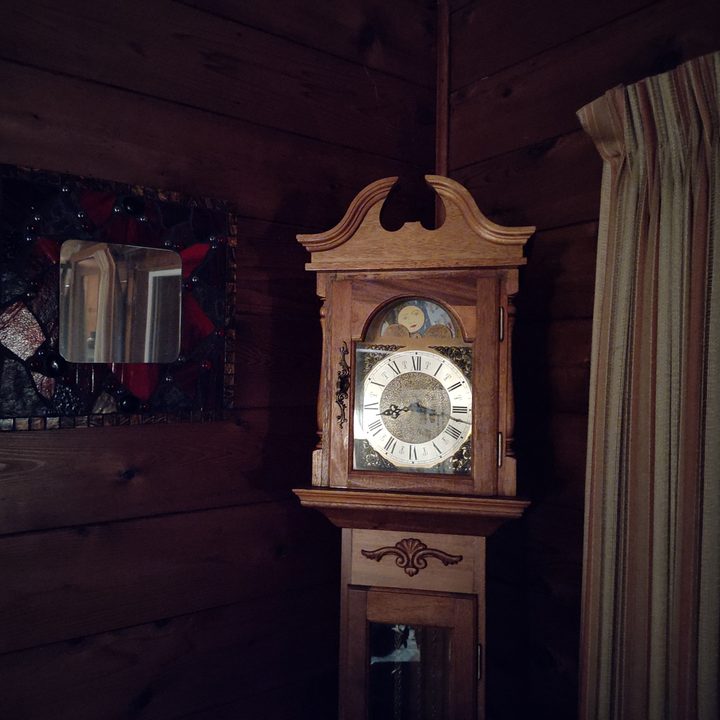 A grandfather clock in the corner of a dark room.