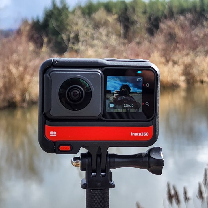 Insta360 One RS with 360 lens. Powered on with an image on the screen and a pond in the background.