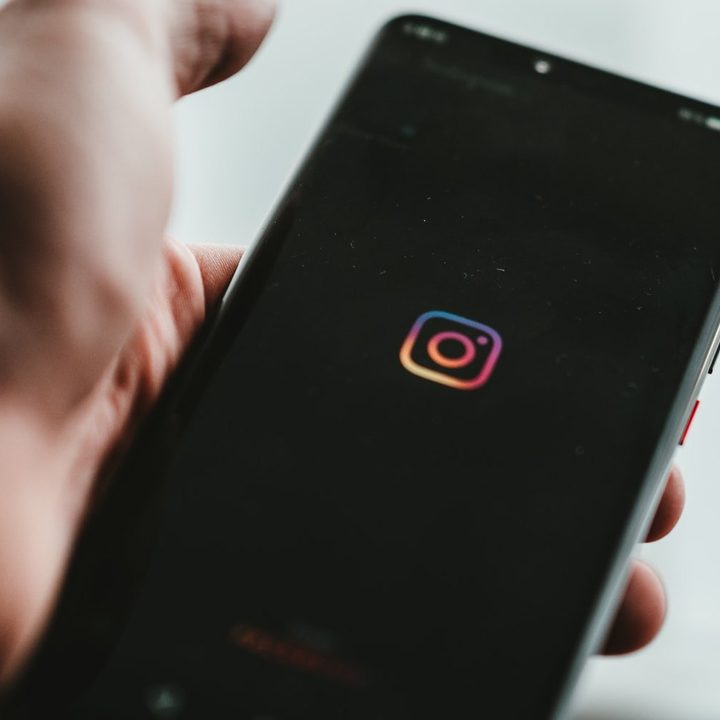 The Instagram mobile app is visible on a phone screen in a man's hand.