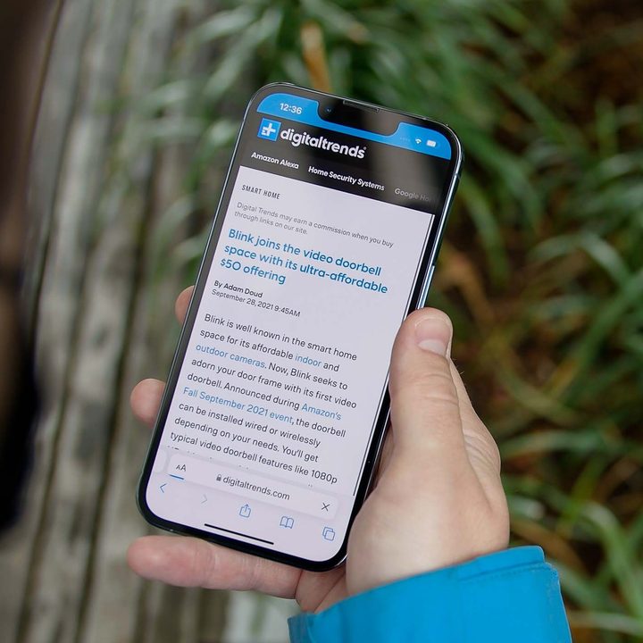 A hand holds an iPhone displaying a Digital Trends news article.