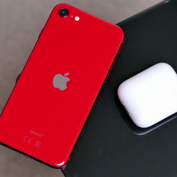 The iPhone SE 2020 on the corner of a table, next to an AirPods case.