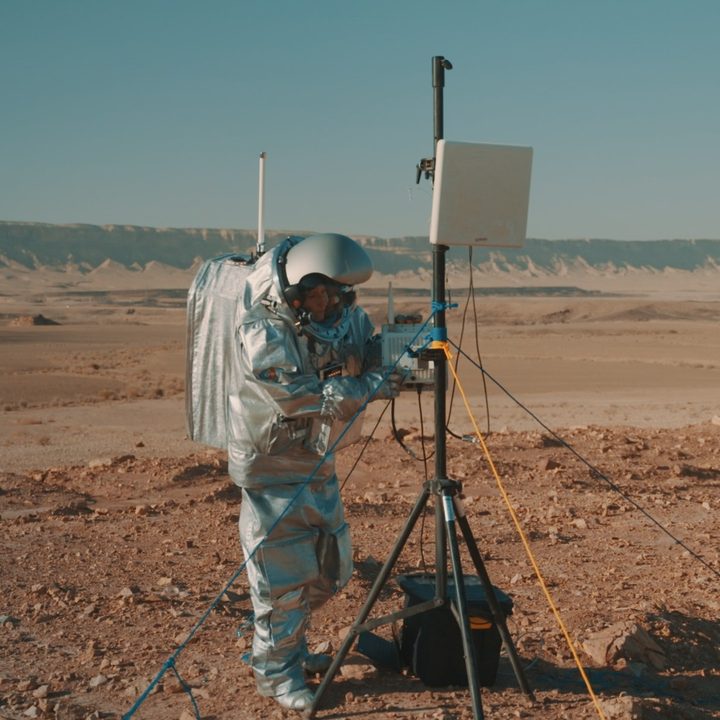 A scientist in an astronaut suit adjusts some research equipment in the desert.