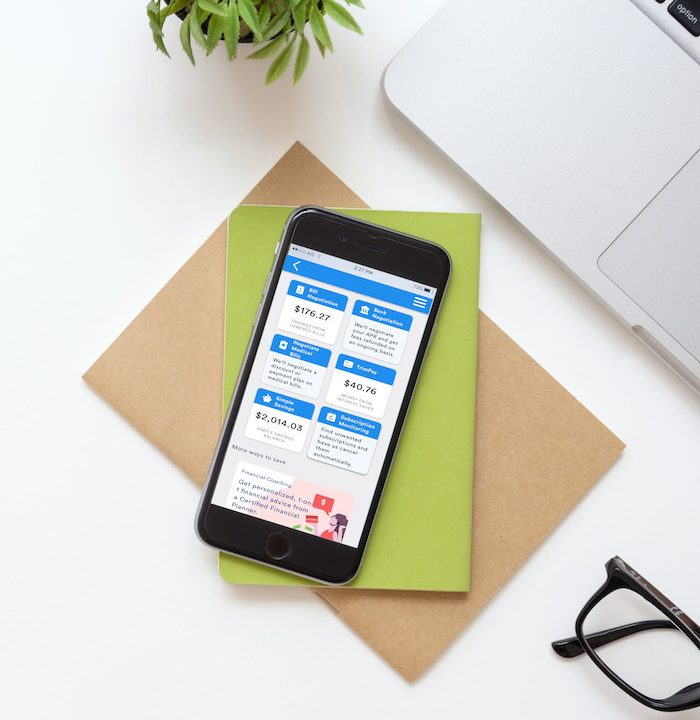 Trim app homepage is visible on a phone sitting on some folders on a desk.