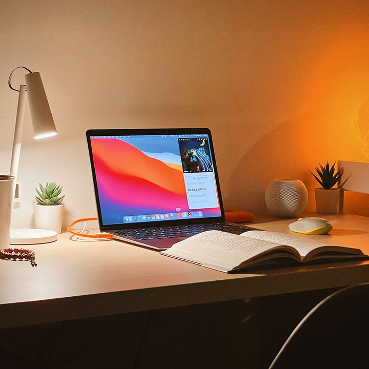 A MacBook Air on a desk with an open book in front of it.