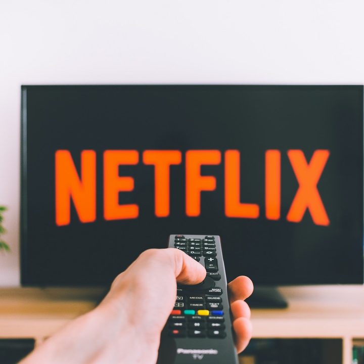 A hand points a remote at a TV display a Netflix logo screen.