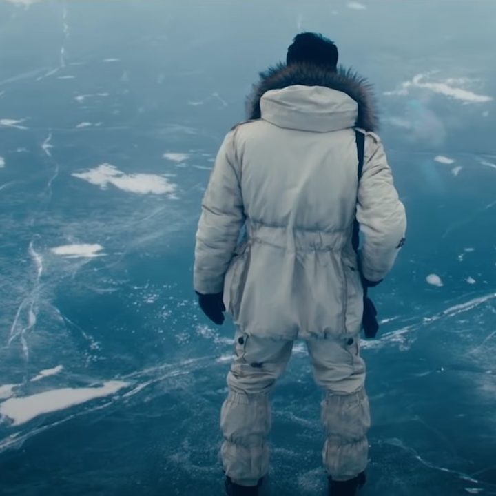 Rami Malek wears a white winter suit as Lyutsifer Safi, standing on an ice lake
