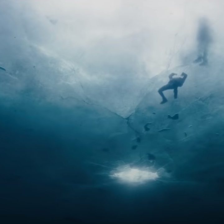 A person swims under the ice of a frozen lake in a scene from No Time To Die.