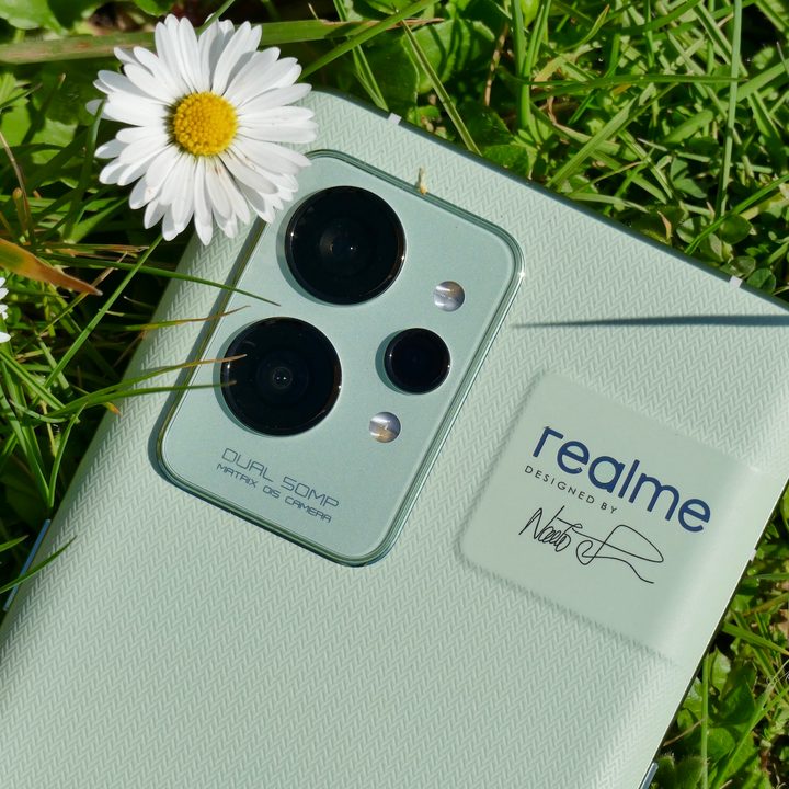 The .Realme GT 2 Pro laying in the grass next to flowers