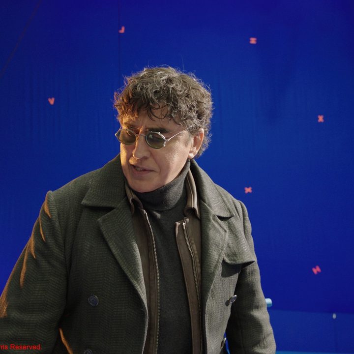 Alfred Molina stands in front of a blue screen in a scene from Spider-Man: No Way Home.