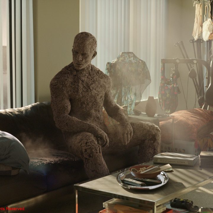 Sandman stares at a pile of sand he left on the couch in a scene from Spider-Man: No Way Home.