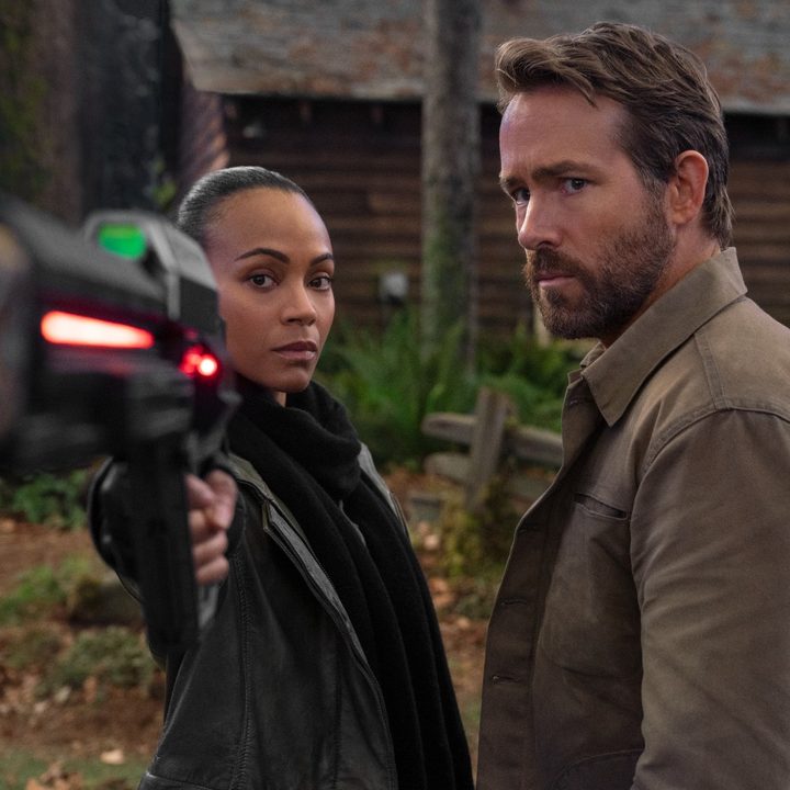 Zoe Saldana points a gun at the camera while standing next to Ryan Reynolds.
