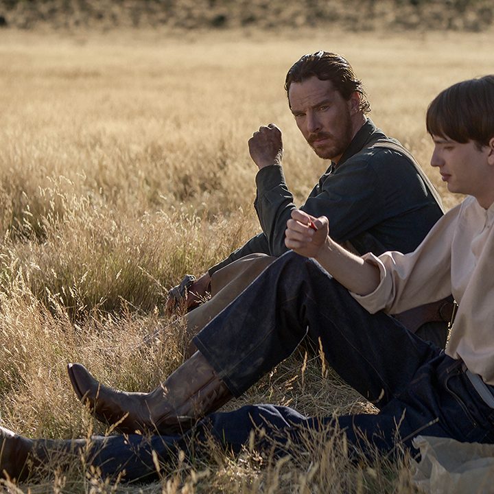 Two men sit in a field in a scene from The Power of the Dog.