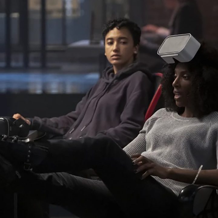 Aleesha, with her feet on a desk, talks with Nora as they work in Upload on Amazon Prime.