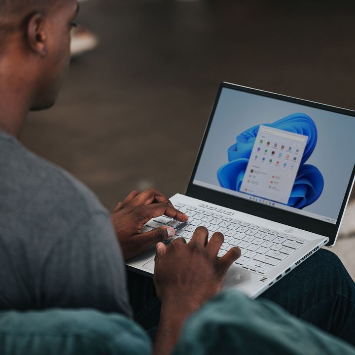 A man sits, using a laptop running the Windows 11 operating system.