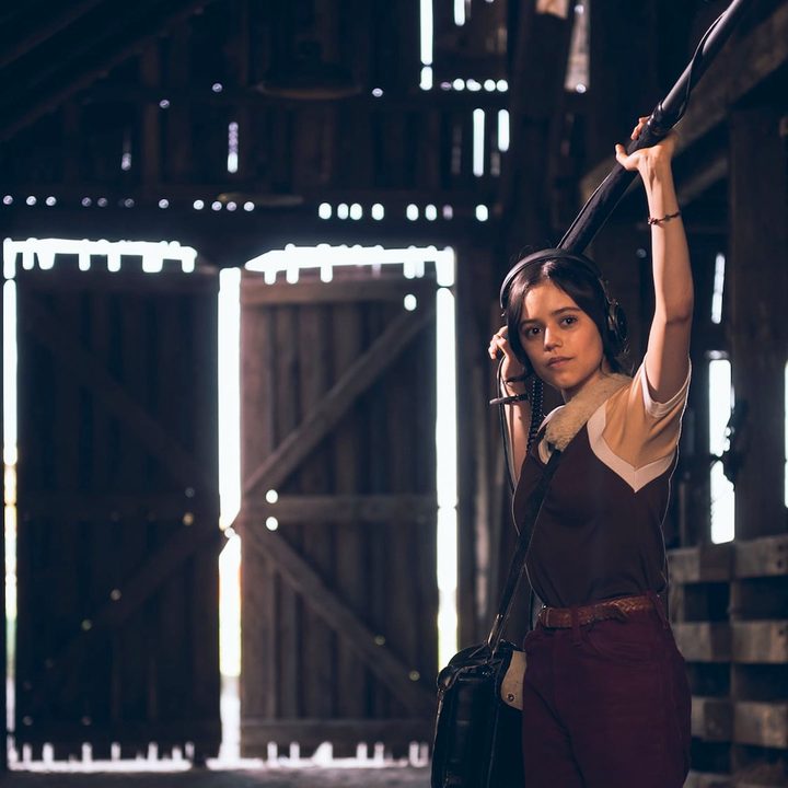 Jenna Ortega holds a boom mike in a barn in X.