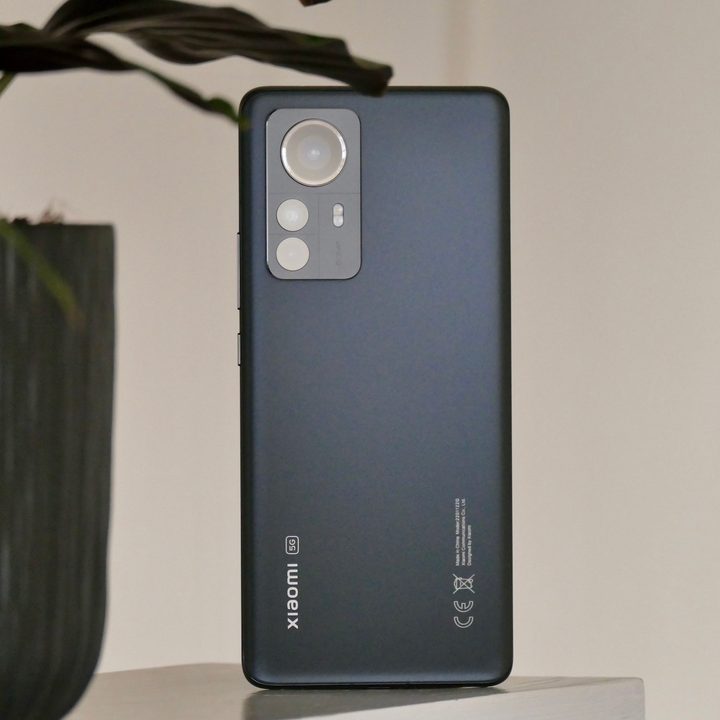 The Xiaomi 12 Pro sits on a ledge next to a plant with the rear panel visible.