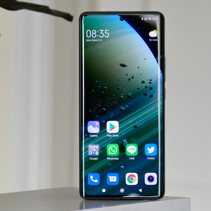The Xiaomi 12 Pro sits on a ledge next to a plant with the display visible.