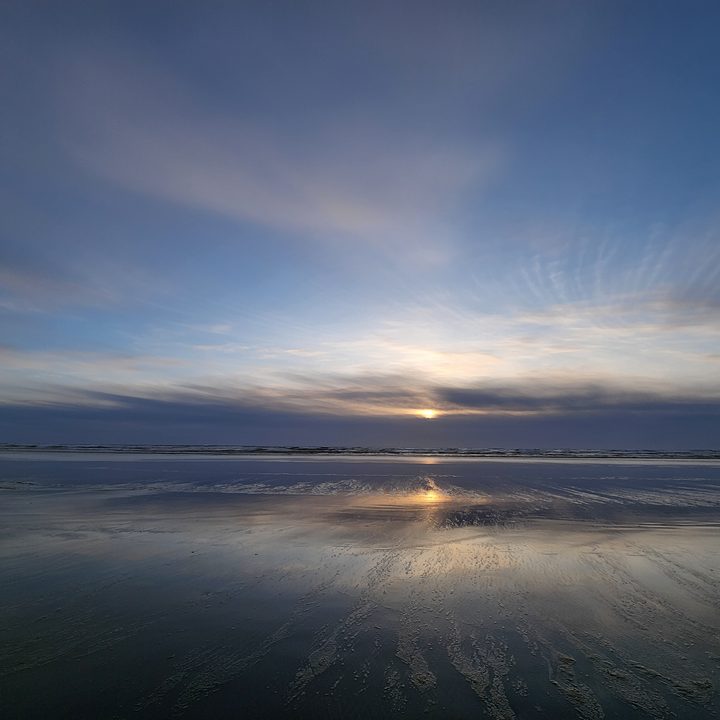 Sunset reflected in wet sand at the edge of the ocean.