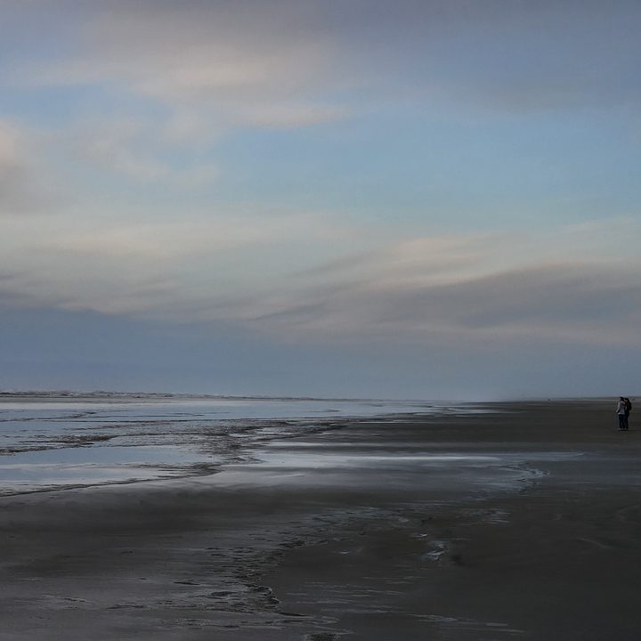 A beach at sunset with two distant people.