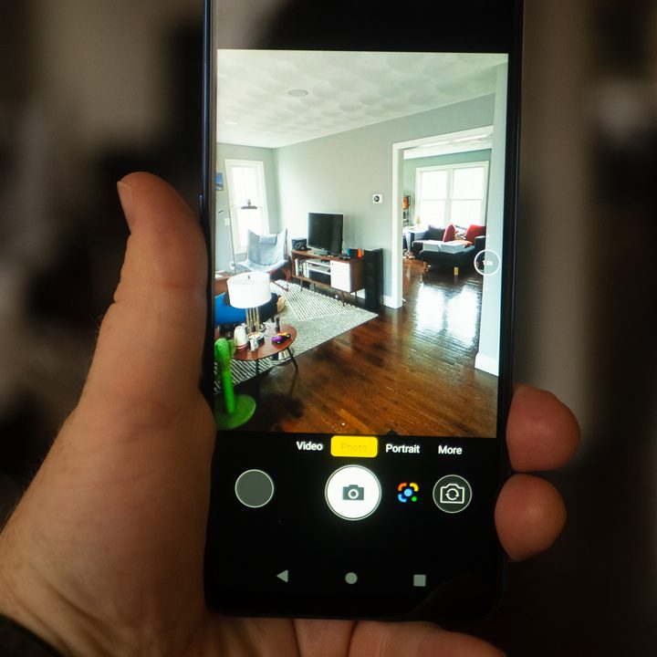 A hand holding a Blu F91 smartphone taking a picture of a living room.