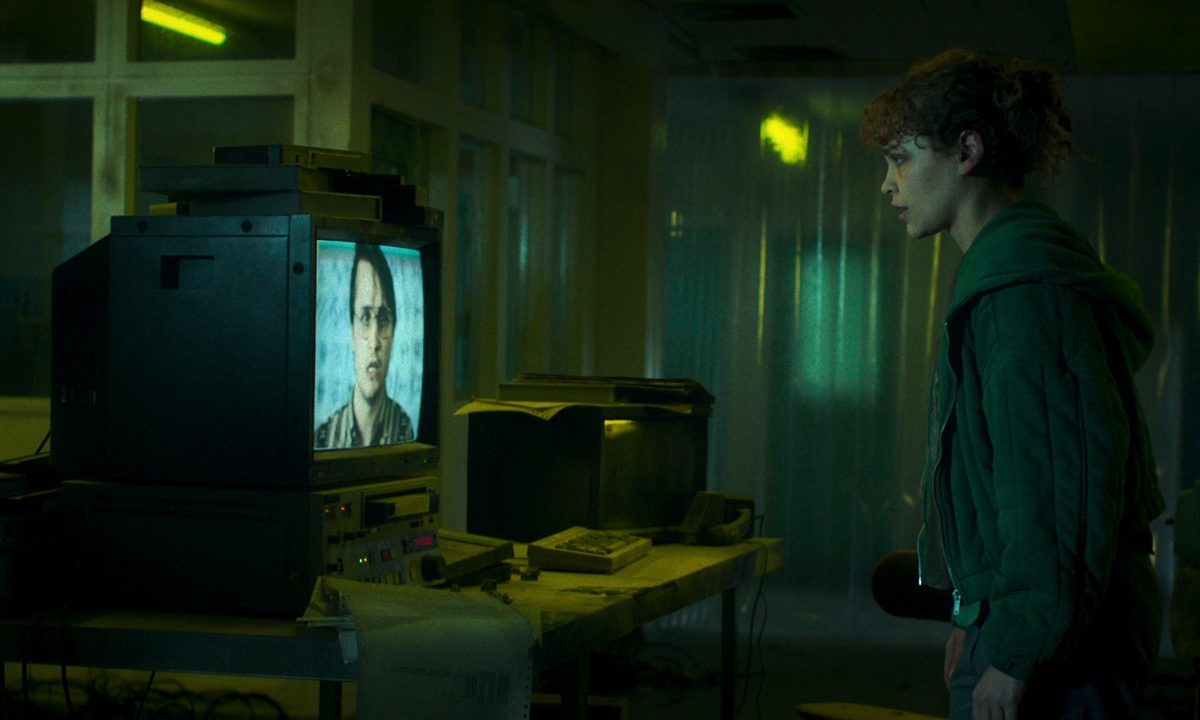 Iola evans stares at a TV screen in a scene from Choose Or Die.