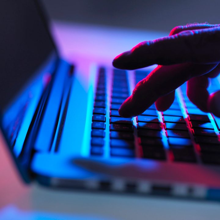 Silhouette of male hand typing on laptop keyboard at night.