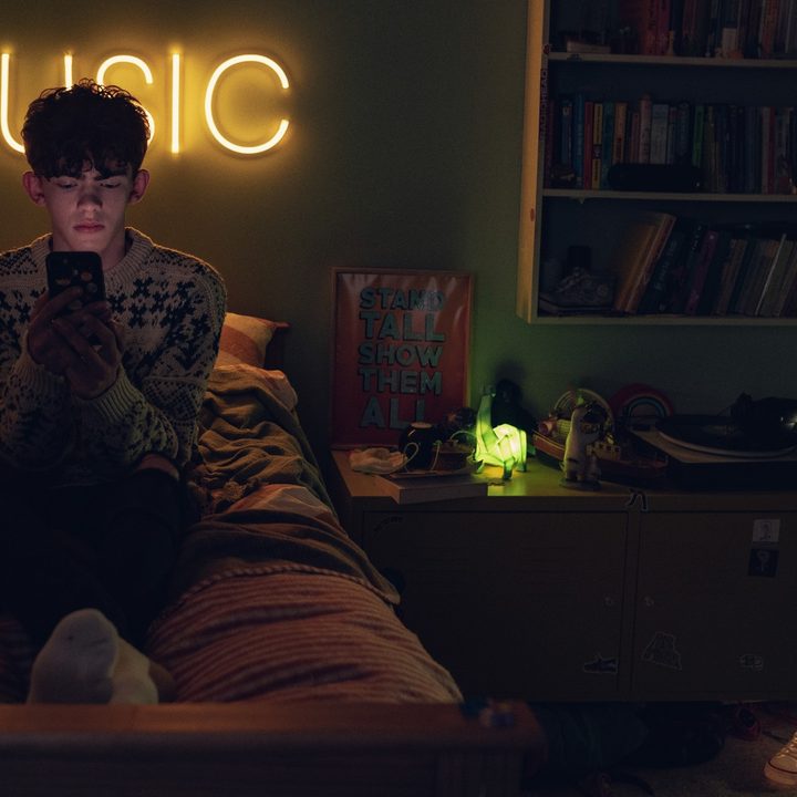 Charlie sits on his bed texting in Heartstopper.