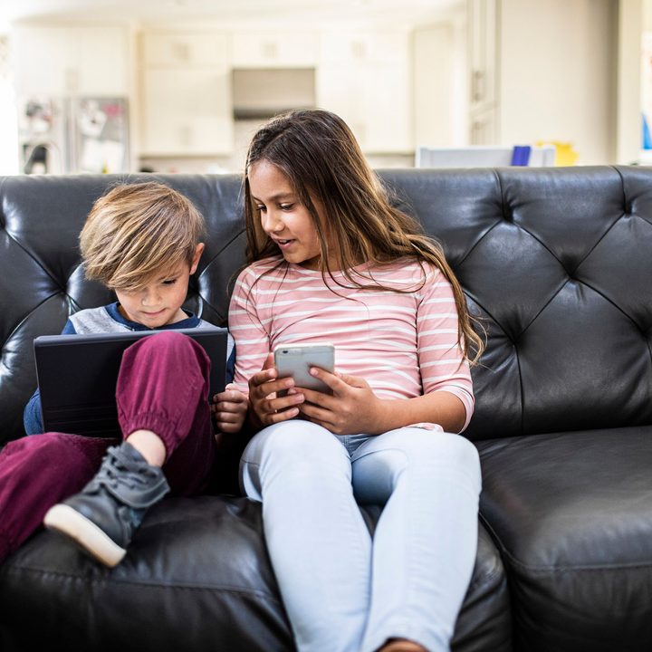 Children using smart devices on sofa at home;