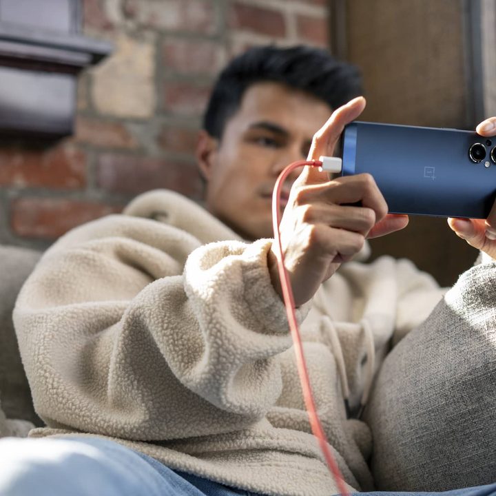 Man relaxing while holding OnePlus Nord N20 phone plugged into charging cable.