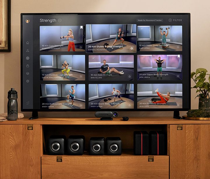 A Peloton Guide placed underneath a tv that shows the Peloton Strength programs.