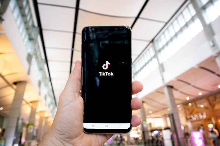 A person's hand holding a phone with the TikTok app on it.