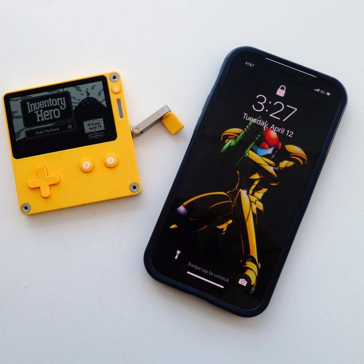 A Playdate sits next to an iPhone 12.