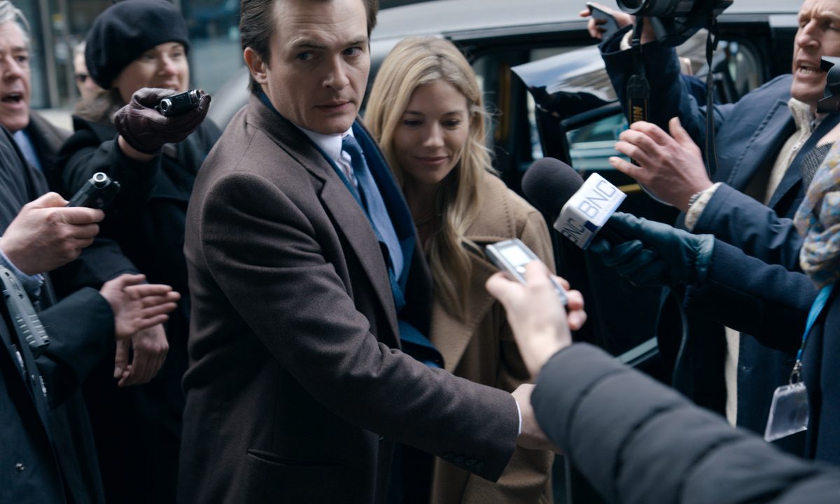 Rupert Friend and Sienna Miller stand in a crowd of reporters in Anatomy of a Scandal.