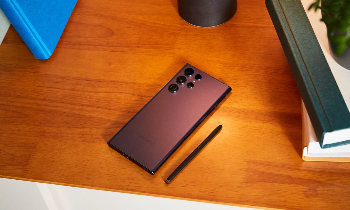 Burgundy colored Samsung Galaxy S22 Ultra placed on a table alongside the S Pen.