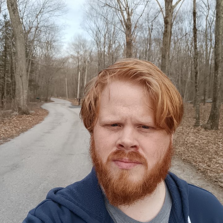 A selfie of a man standing on a country road in the woods
