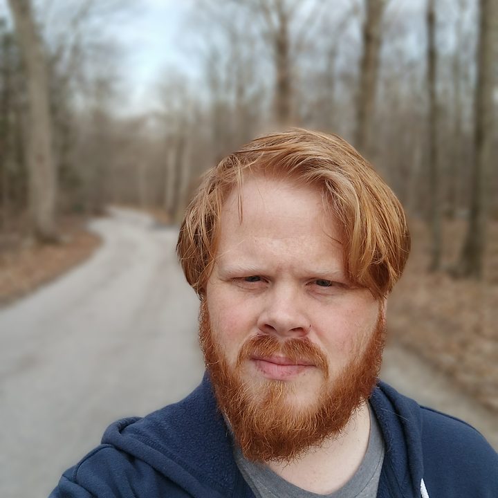 A selfie of a man standing on a country road in the woods with a blurred background