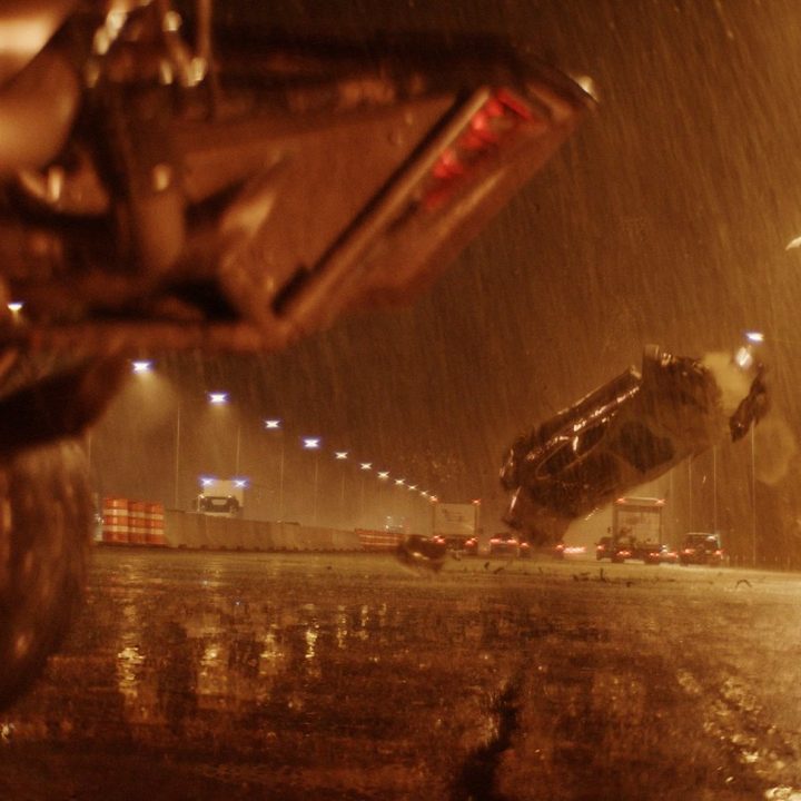 A car crashes in the background on a highway in a scene from The Batman.