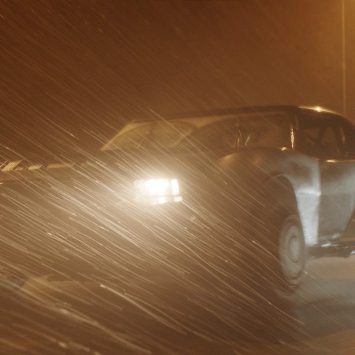 The Batmobile roars down a rainy street in a scene from The Batman.