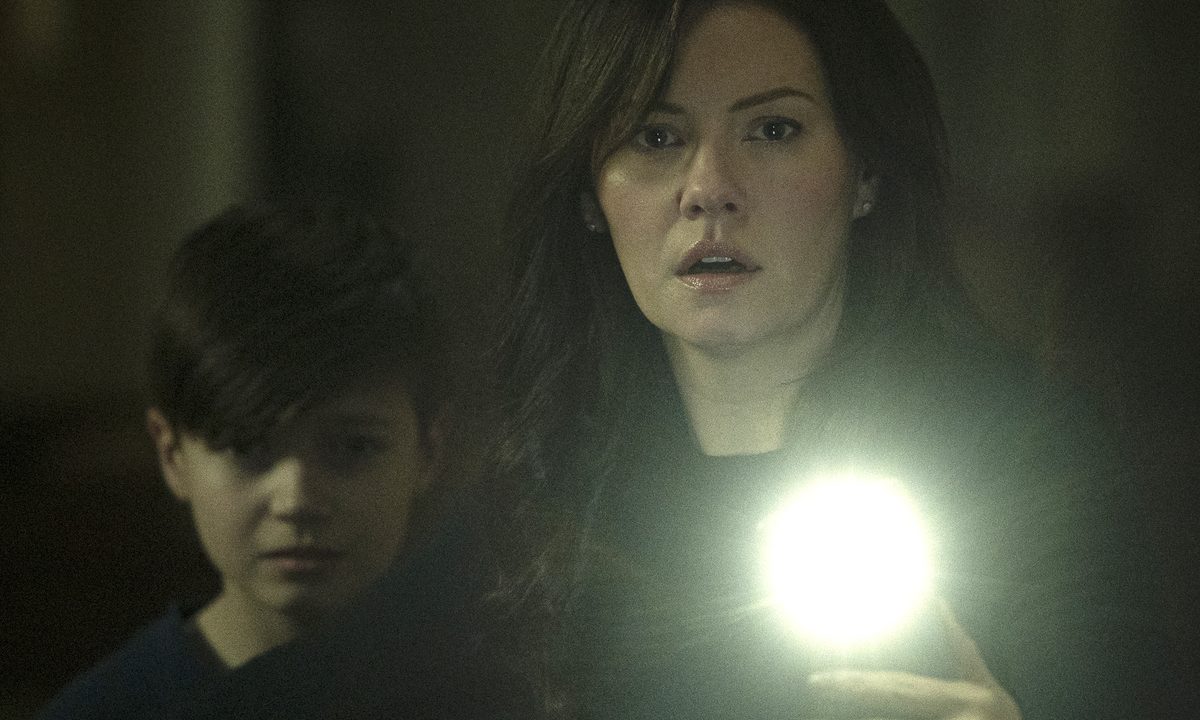 Keira holds a light up with Steven standing behind her in a scene from The Cellar.