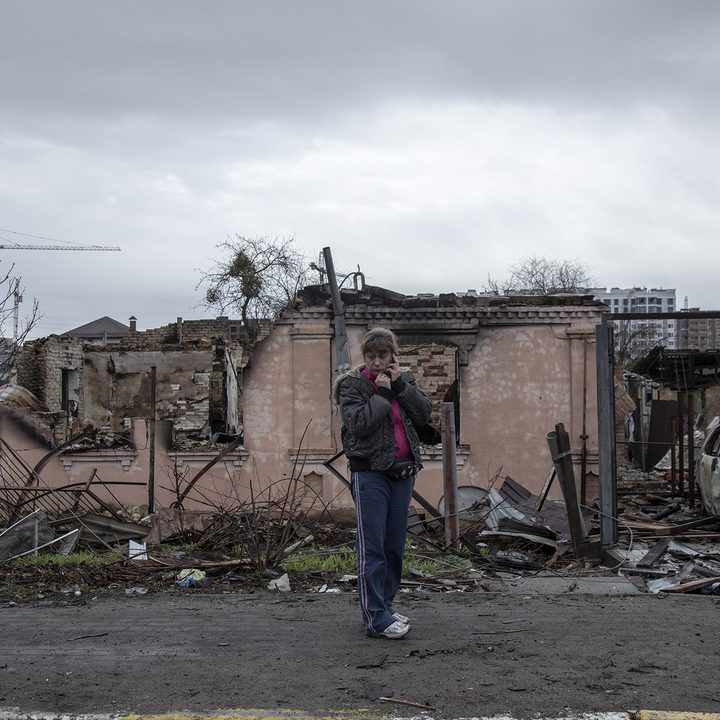 During the 2022 Russian attacks on Ukraine, a woman stands in the rubble while talking on the phone.