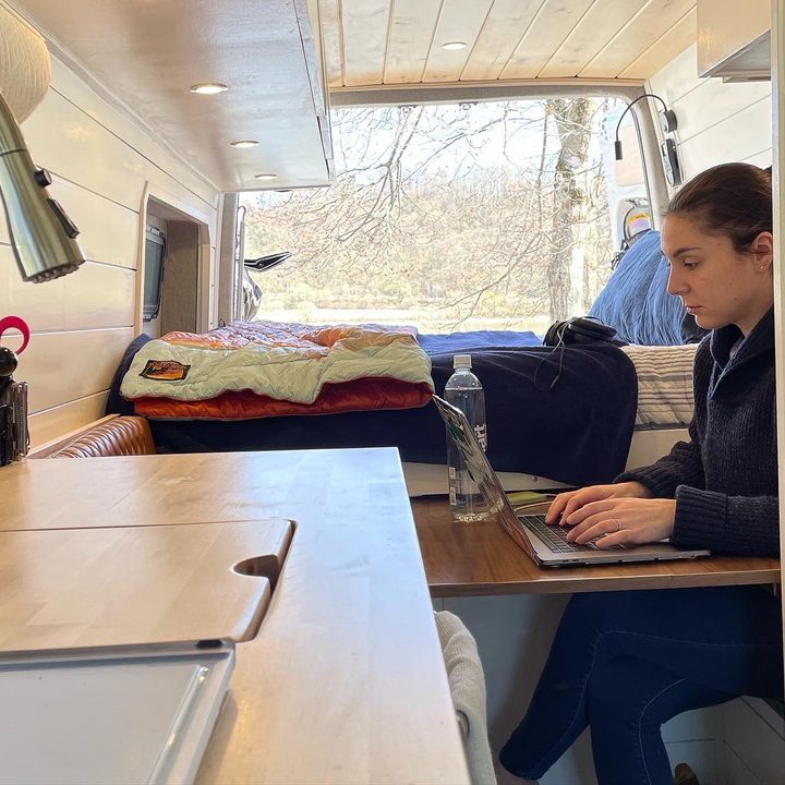 A woman sitting at a foldout table working on a laptop in a van